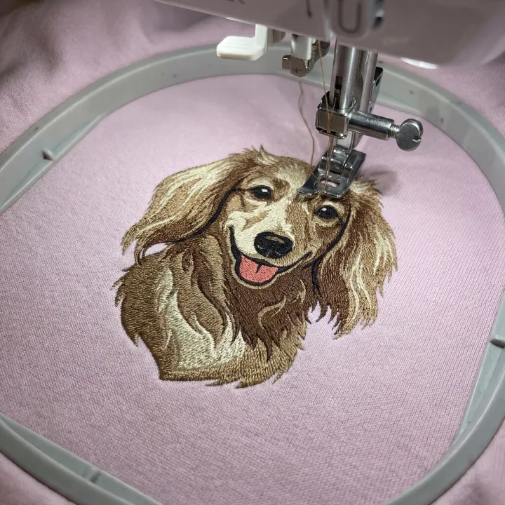 A pet design being embroidered onto a pink sweatshirt